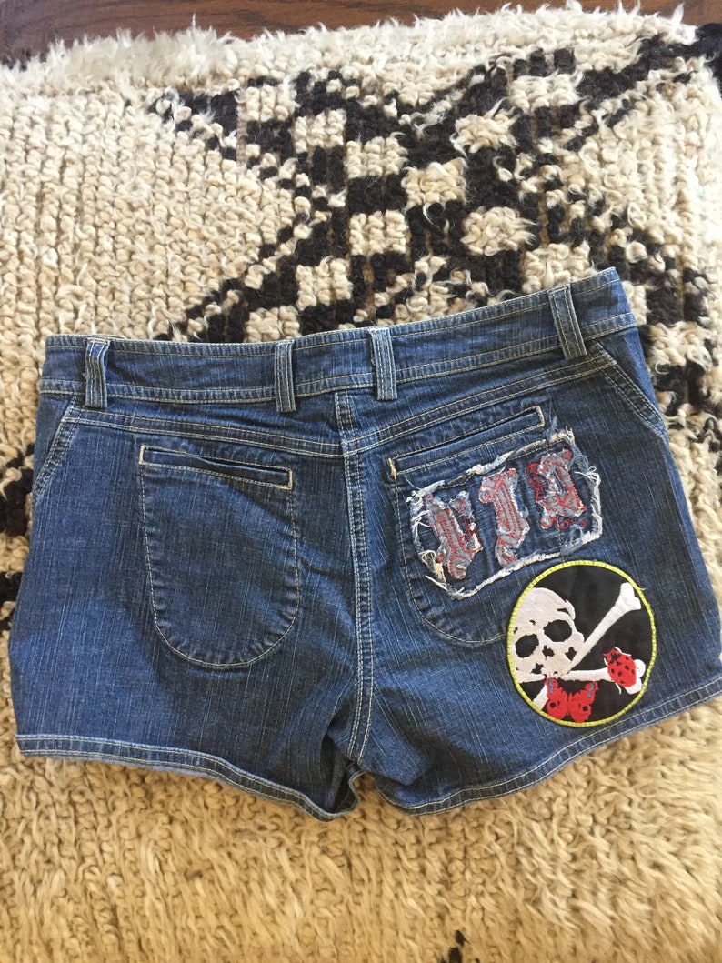 May include: Blue denim shorts with a skull and crossbones patch and a distressed patch that says "VIP" on the back.