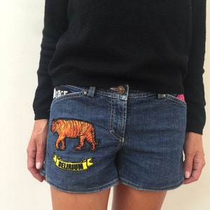 May include: Blue denim shorts with a tiger and the word "Delirium" embroidered on the front pocket.