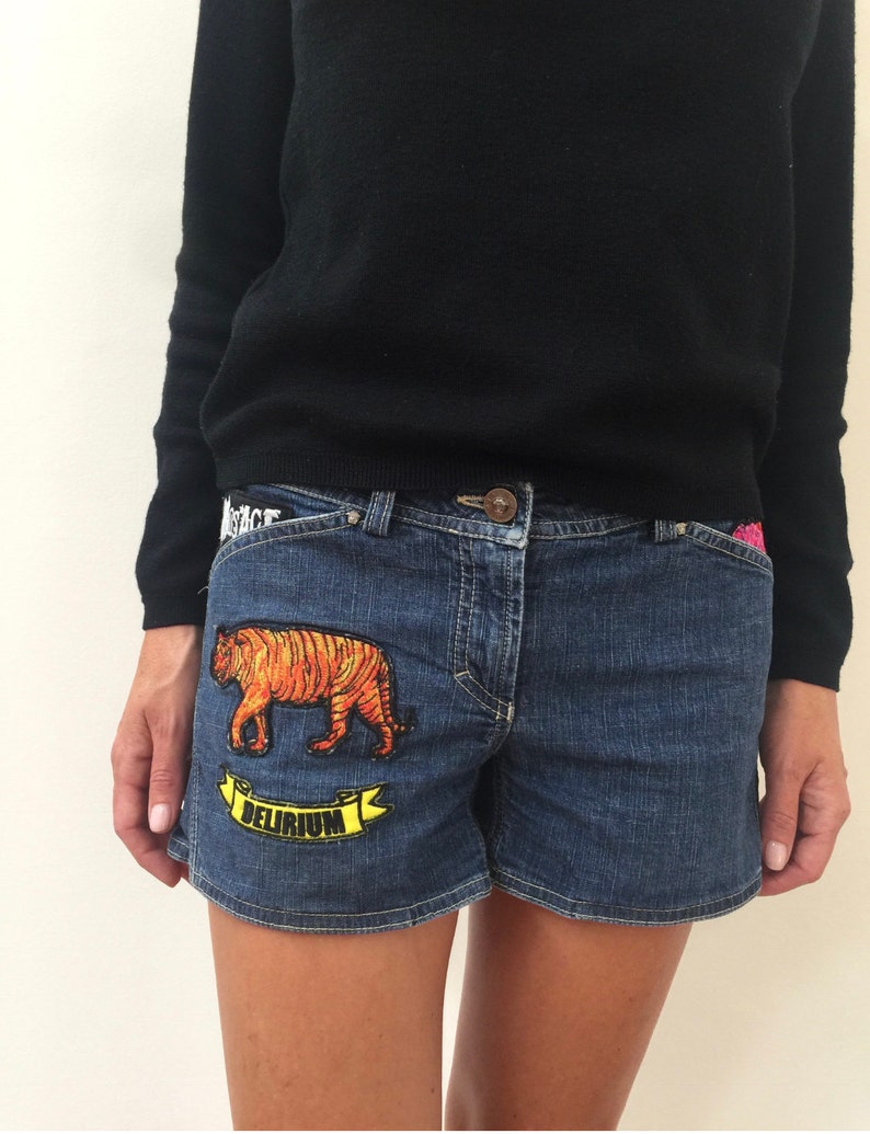 May include: Blue denim shorts with a tiger and the word "Delirium" embroidered on the front pocket.