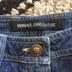 May include: Blue denim jeans with a black label that reads "VERSACE JEANS COUTURE" and a silver button with the same text.