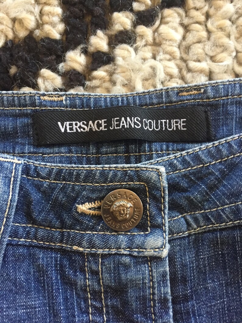 May include: Blue denim jeans with a black label that reads "VERSACE JEANS COUTURE" and a silver button with the same text.