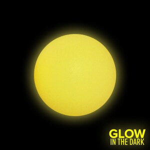 Op de afbeelding: Een heldergele glow-in-the-dark bal. De bal is rond en glad. De tekst "GLOW IN THE DARK" is in het geel onder de bal gedrukt.