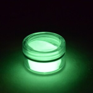 May include: A small, round jar filled with a bright green glow-in-the-dark powder. The jar is made of clear glass and has a black lid.