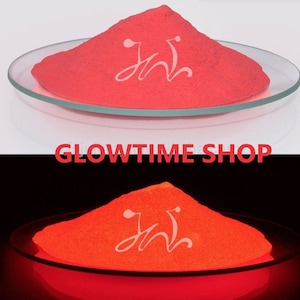May include: A pile of bright red glow-in-the-dark powder in a white dish. The powder glows a bright orange in the dark.