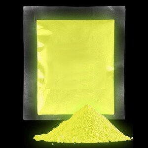 Op de afbeelding: Een verzegelde zak met felgeel glow-in-the-dark poeder. Het poeder stroomt uit de zak en vormt een kleine hoop op een zwart oppervlak.