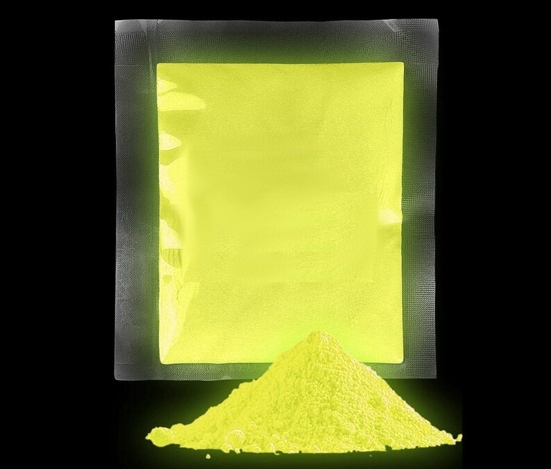 Op de afbeelding: Een verzegelde zak met felgeel glow-in-the-dark poeder. Het poeder stroomt uit de zak en vormt een kleine hoop op een zwart oppervlak.