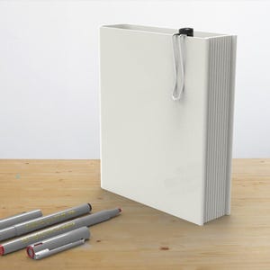 May include: A white blank notebook with a silver bookmark and four silver and gray pens on a wooden surface.