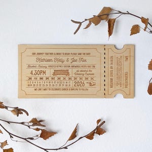 May include: A laser-cut wooden wedding invitation in the style of a train ticket. It features the names Kathleen Kelly & Joe Fox, the date, time, and location of the wedding. The design includes a train illustration and the words "Wedding Express."