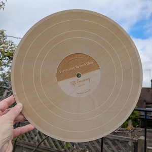 May include: A wooden record-shaped plaque commemorating the fifth anniversary of Preserving Record Shop in New Kensington, PA. The plaque is brown and has a light brown centre with the text "Fifth Anniversary April 2021 New Kensington, PA".