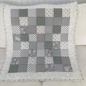 May include: A white baby quilt with a grey patchwork design. The quilt is made up of squares of different grey fabrics with white polka dots, floral patterns, and geometric designs.