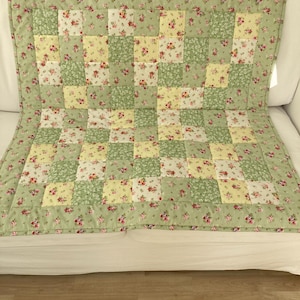 May include: A green and yellow patchwork quilt with a floral pattern. The quilt is made of squares of fabric sewn together.