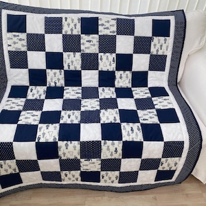 May include: A patchwork quilt in navy blue, white, and grey, with a checkerboard design. The quilt has squares of solid navy, white with navy polka dots, and white with grey cat silhouettes. A navy border with white polka dots frames the quilt.