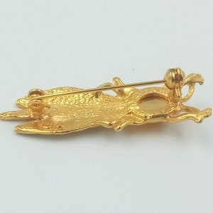 May include: Gold-toned brooch in the shape of a stylized bird with a round, clear stone in the center. The brooch has a pin and catch closure on the back.