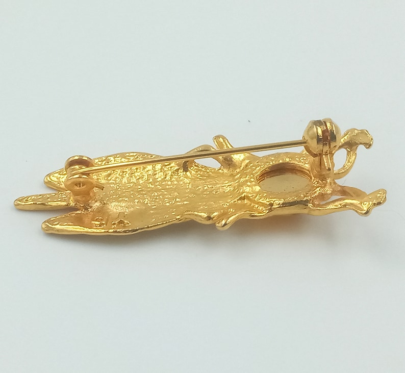 May include: Gold-toned brooch in the shape of a stylized bird with a round, clear stone in the center. The brooch has a pin and catch closure on the back.