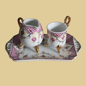 Peut inclure: Un ensemble de thé en porcelaine miniature avec un motif floral rose et blanc. L'ensemble comprend une crémier, une tasse et un petit plateau.