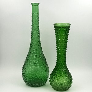 Può includere: Due vasi di vetro verde con superficie testurizzata. Il vaso a sinistra è a forma di pera e il vaso a destra è alto e sottile.
