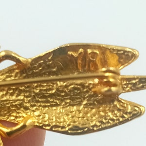 May include: Gold-toned metal dragonfly brooch with a textured surface and the inscription "VRI" on the back.