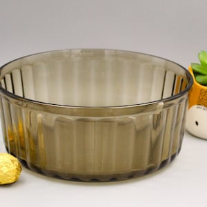 May include: A brown glass baking dish with fluted sides. The dish is empty and sitting on a white surface. There are three gold-wrapped chocolate candies in the foreground.