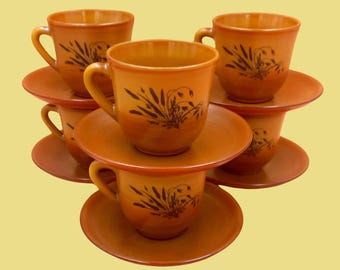 May include: Set of six brown ceramic teacups and saucers with a floral design. Each cup and saucer features a black floral pattern with a brown background.