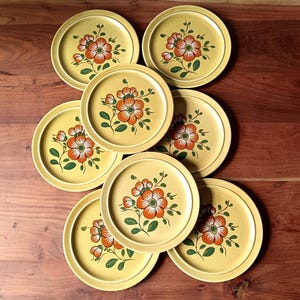 Peut inclure: Ensemble de huit assiettes en céramique jaune, décorées d'un motif floral. Chaque assiette présente une fleur orange avec des détails blancs et verts. Les assiettes sont disposées sur une surface en bois.