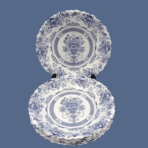 May include: A stack of four white ceramic dinner plates with a blue and white floral pattern. The plates have a scalloped edge and a raised rim.