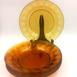 May include: A set of six amber glass dinner plates with a textured rim. The plates are stacked on top of each other.