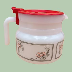 May include: White jug with a red lid and floral design. The jug has a handle and a spout.