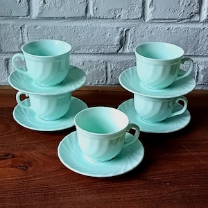 May include: A set of six light blue teacups and saucers. Each cup has a curved handle and sits on a matching saucer. The cups and saucers have a spiral design. The set is arranged on a wooden surface.