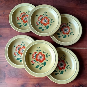 Peut inclure: Six assiettes en céramique beiges avec un motif floral. Chaque assiette présente un groupe central de fleurs orange avec des feuilles vertes. Les assiettes sont disposées sur une surface en bois foncé, mettant en valeur une esthétique vintage.