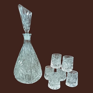 Peut inclure: Un ensemble de six verres à liqueur en verre transparent et une carafe en cristal avec un motif facetté. La carafe a un bouchon avec un sommet pointu.