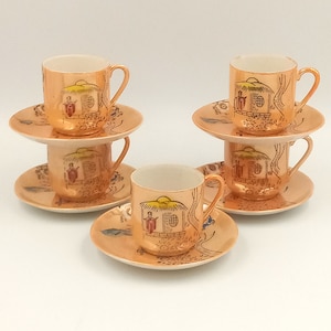 Könnte beinhalten: Set aus vier goldgeränderten Porzellan-Teetassen und Untertassen mit einem zarten asiatisch inspirierten Design. Jede Tasse und Untertasse zeigt ein kleines Haus mit einem Strohdach und einer Figur, die davor steht. Das Design ist in Braun-, Gelb- und Rottönen gemalt.