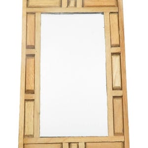 May include: Rectangular wooden mirror with a light brown frame. The frame has a geometric design with rectangular and square accents. The mirror's reflective surface is clear and smooth, suitable for home decor.