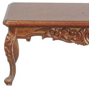 Puede incluir: Una mesa de centro de madera marrón oscuro con tallas ornamentadas en el faldón y las patas. La mesa tiene una tapa rectangular y un faldón ligeramente curvado.