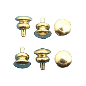 May include: Six small, shiny, gold-colored furniture knobs. Three knobs have a stem and a rounded top, while the other three are round with a flat bottom. The knobs are likely for drawers or cabinets.