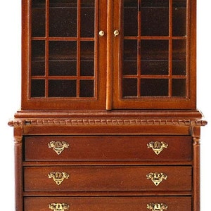 Op de afbeelding: Miniatuur houten kast met glazen deuren en vier laden. De kast heeft een diepbruine kleur met goudkleurige hardware. Het bovenste gedeelte heeft gebogen glazen ruiten. De kast is een poppenhuis-groot meubelstuk.