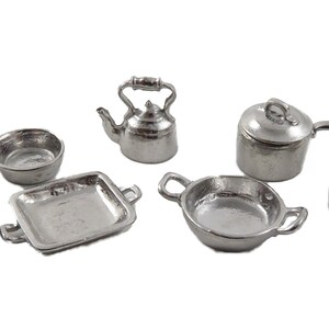 Peut inclure: Un ensemble de cuisine miniature en argent, comprenant une théière, deux casseroles avec couvercles, une poêle, une casserole et un plat à four.