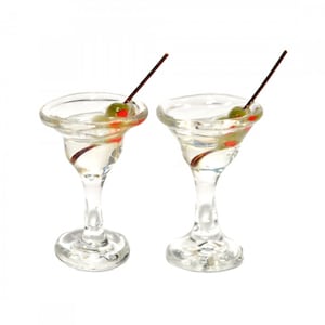 Op de afbeelding: Twee heldere martini glazen gevuld met een heldere vloeistof, elk gegarneerd met een groene olijf en een plakje rode peper op een houten prikker. De glazen hebben een uitlopende rand en een voet, tegen een witte achtergrond.