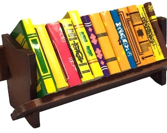 May include: A miniature wooden bookshelf with a brown finish, holding a collection of colorful miniature books. The books have various patterns and designs, including floral, geometric, and abstract.