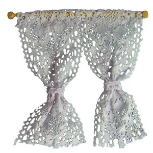 May include: A pair of white crocheted curtains with a wooden rod at the top. The curtains are tied back with bows.