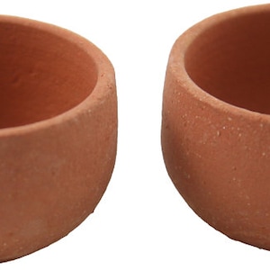May include: Two terracotta clay cups, each with a rounded bottom and a smooth, slightly textured surface. The cups are empty and appear to be handmade.