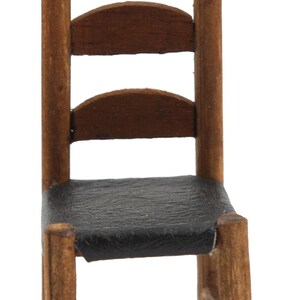 May include: A wooden chair with a black leather seat. The chair has a simple design with four legs and a back with three horizontal slats.