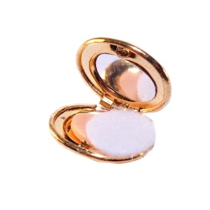 Puede incluir: Un espejo compacto dorado con un interior blanco y esponjoso. El espejo está abierto y la tapa está levantada.