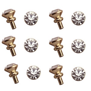 May include: Twelve gold-toned cabinet knobs with clear crystal accents. Each knob has a round base and a small, round, raised crystal in the center.