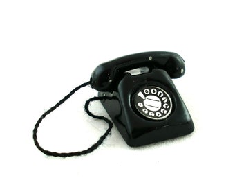 May include: A black rotary dial phone with a black cord. The phone has a white dial with black numbers.