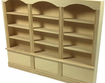 Puede incluir: Una estantería de madera con tres secciones, cada una con cuatro estantes. Los estantes tienen un acabado de madera clara y son arqueados en la parte superior. La estantería es independiente y tiene una base con tres paneles.