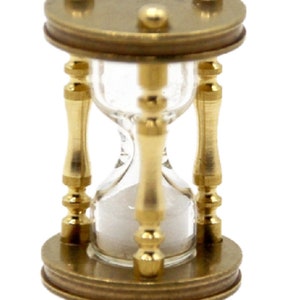 May include: A small brass hourglass with a clear glass bulb. The hourglass is approximately 10 cm tall and has a gold finish.
