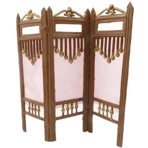 May include: A three-panel room divider made of wood with a pink fabric insert. The divider has a decorative design with gold accents and a scalloped top.