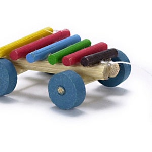 May include: A wooden toy xylophone with colourful wooden bars on a small wooden wagon with blue wheels. The wagon has a string attached to a black ball.