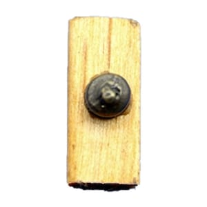 Puede incluir: Un botón pequeño, redondo, de color latón con un diseño en relieve está unido a una pieza rectangular de madera marrón claro.