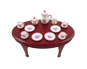 May include: A miniature tea set with a pink and white floral design on a red wooden table. The set includes a teapot, creamer, sugar bowl, and six teacups and saucers.